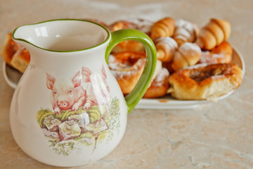 buns in a plate full of freshly baked bagels dusted with icing sugar with a ceramic jug on the kitchen table. cooking baking. croissants baking preparation stage. breakfast closeup copy space