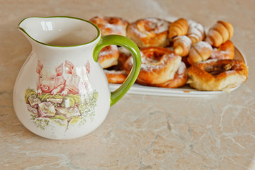 buns in a plate full of freshly baked bagels dusted with icing sugar with a ceramic jug on the kitchen table. cooking baking. croissants baking preparation stage. breakfast closeup copy space