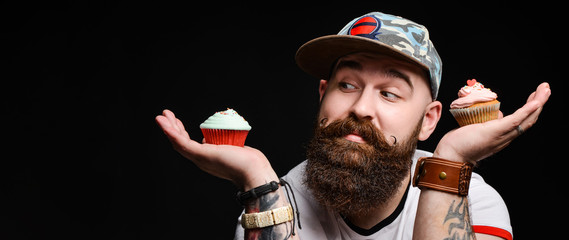 Happy bearded bald man holding two cream cakes on black background.