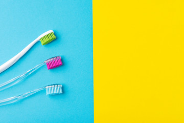 Three plastic toothbrushes on a colorful blue and yellow  background, close up