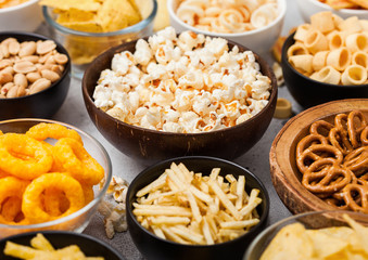 All classic potato snacks with peanuts, popcorn and onion rings and salted pretzels in bowl plates...