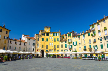 Piazza dell Anfiteatro square in circus yard of medieval town Lucca historical centre, old colorful buildings with shutter windows and blue clear sky copy space background, Tuscany, Italy - obrazy, fototapety, plakaty