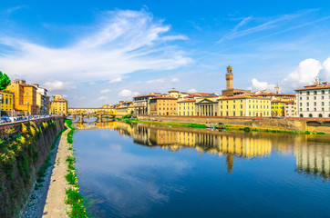 Ponte Vecchio bridge with colourful buildings houses over Arno River blue reflecting water and embankment promenade in historical centre of Florence city, blue sky white clouds, Tuscany, Italy