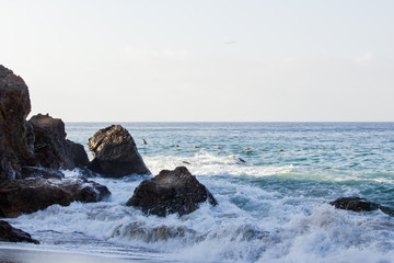 crashing wave foaming past early morning lit boulders frothing on the beach