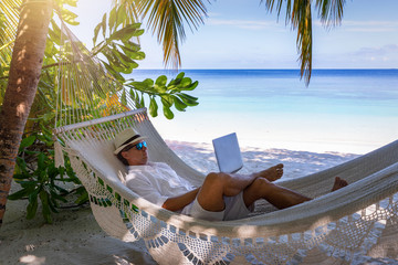 Arbeiten im Urlaub: Mann mit Laptop auf Hängematte am tropischen Strand unter Palmen