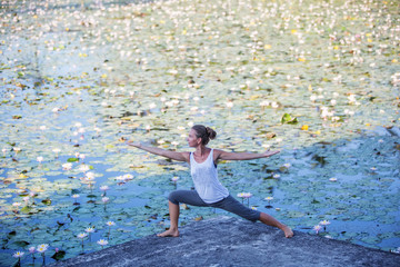 Woman practices yoga on a lake with lotus water lilies