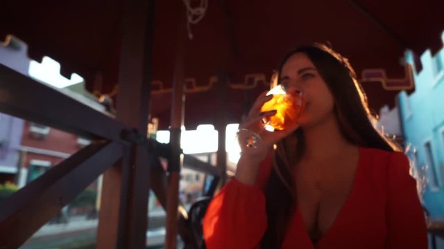 Girl drinks a cocktail spritz aperol in a cold glass in a warm Sunny day in a street cafe. Sunset