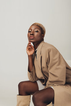 elegant african american woman in beige jacket sitting on chair isolated on grey