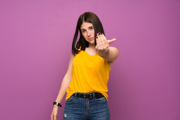 Young woman over isolated purple wall inviting to come with hand. Happy that you came