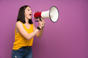 Young woman over isolated purple wall shouting through a megaphone