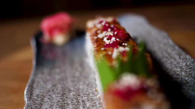 Сlose up for sushi rolls on black tray standing on the table, Japanese traditional food. Frame. Delicious decorated rolls lying on a plate with pink ginger.