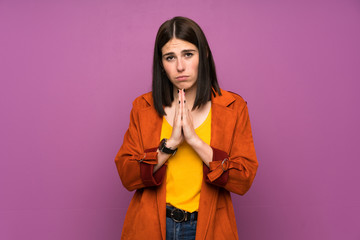 Young woman with a coat over isolated purple background pleading