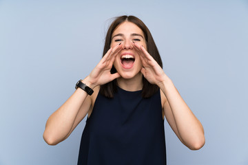 Young woman over isolated blue wall shouting with mouth wide open