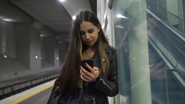 A young woman in a subway using her cell phone. The girl waits for the train and touches the mobile phone. Internet connection on the railway station