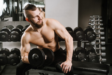 Fototapeta na wymiar Strong man sitting and lifting dumbbells in the gym