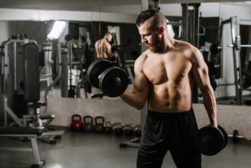 Fototapeta na wymiar Muscular strong man doing exercises with a dumbbells in the gym