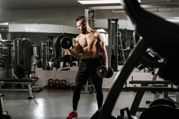 Fototapeta na wymiar Muscular strong man doing exercises with a dumbbells in the gym
