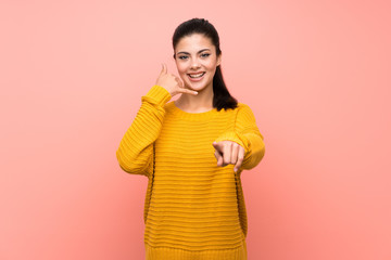 Teenager girl  over isolated pink wall making phone gesture and pointing front