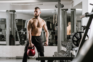 Naklejka premium Muscular man doing exercises with a big dumbbell in the gym