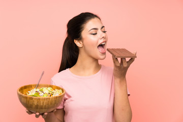 Teenager girl  over isolated pink wall with salad and chocolat