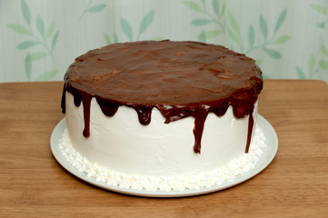 Birthday cake with chocolate syrup. Decorated with flowers made with frosting bag. Background with leaf design on white curtain. Horizontal.