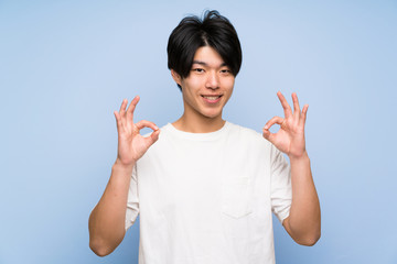 Asian man on isolated blue background showing an ok sign with fingers