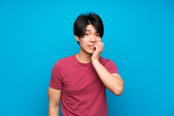 Asian man with red shirt over isolated blue wall nervous and scared