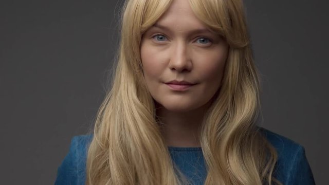 blue eued nordic model in studio closeup portrait touches her long blonde hair shake head and smiling to the camera