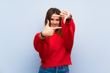 Young woman over isolated blue wall focusing face. Framing symbol