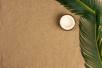  Beach theme on the sand background. Palm leaves, coconut on the sand. Top view.