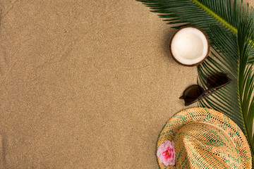 Fototapeta na wymiar Beach theme on the sand background. Palm leaves, coconut, sunglasses on the sand. Top view.