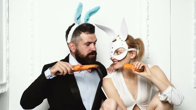 Fitness and Healthy food. Diet. Dieting concept. Healthy Food. Beautiful young woman and bearded man in bunnies mask eat carrots like a rabbit. Food for thought. Pair in bunny masks isolated on white.
