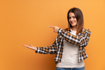 Young woman over brown wall holding copyspace imaginary on the palm to insert an ad