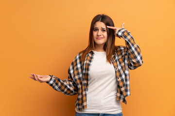 Young woman over brown wall making the gesture of madness putting finger on the head