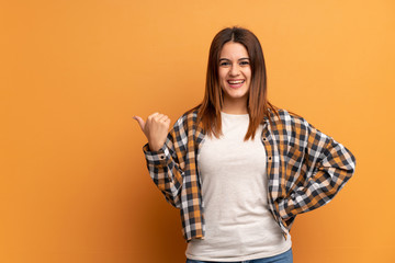 Young woman over brown wall pointing to the side to present a product