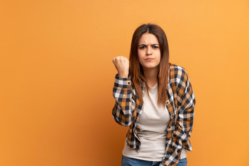 Young woman over brown wall with angry gesture