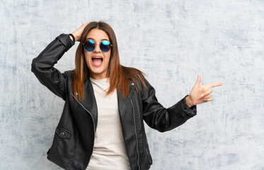 Young woman over textured wall pointing finger to the side and presenting a product