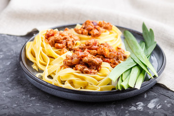 Tagliatelle bolognese pasta with minced meat on a black concrete background.