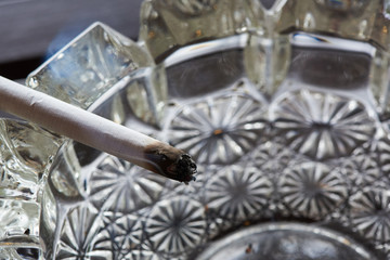 A cigarette and smoke on the glass ashtray
