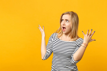 Disgusted shocked young woman in striped clothes looking aside, spreading hands, screaming isolated on yellow orange wall background. People sincere emotions, lifestyle concept. Mock up copy space.