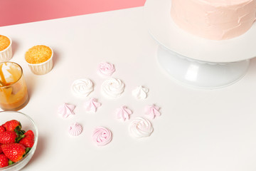 Chef cook confectioner baker white table isolated on pink pastel background in studio. Nude cake with sweet rose cream without decoration, meringue pavlova. Mock up copy space food concept. Nobody.