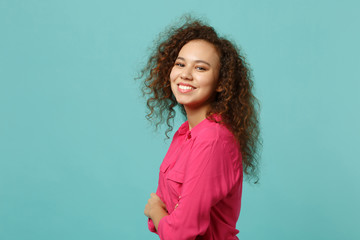 Side view of smiling african girl in pink casual clothes holding hands crossed isolated on blue turquoise wall background in studio. People sincere emotions, lifestyle concept. Mock up copy space.