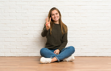 Fototapeta na wymiar Young woman sitting on the floor happy and counting three with fingers