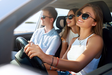 Group of friends rented a car on summer road trip and arrived to the sea beach. Girl having fun with friends in vehicle. Woman in glasses learned driving and got a driver license. Travel lifestyle.