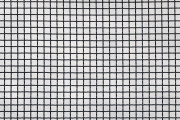 Surface of a latticed metal fence with squares elements in front of a wall made of wire; patterned...