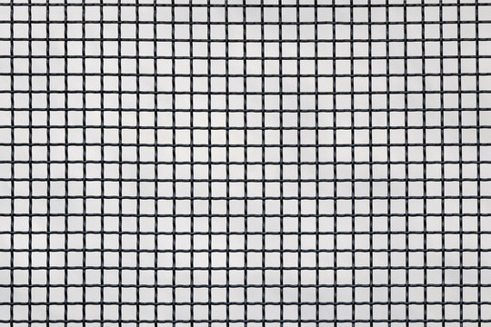 Surface of a latticed metal fence with squares elements in front of a wall made of wire; patterned weave. Metal lattice over the wall as a background texture. Selective focus. Copy space.