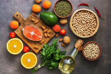 Healthy balanced food, salmon,legumes, fruits, vegetables, olive oil and nuts, dark rustic background. Overhead view, flat lay.