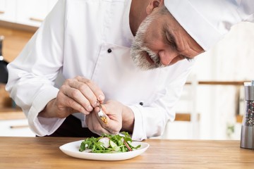 male cook chef decorating garnishing prepared salad dish on the plate in restaurant commercial kitchen.