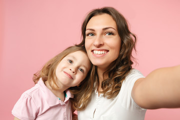 Close up selfie shot woman in light clothes have fun with cute child baby girl. Mother, little kid daughter isolated on pastel pink wall background, studio portrait. Mother's Day, love family concept.
