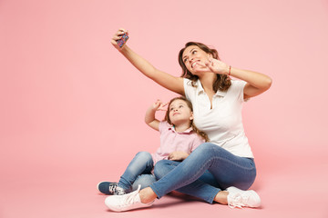 Woman in light clothes have fun with cute child baby girl. Mother, little kid daughter isolated on pastel pink wall background, studio portrait. Mother's Day, love family, parenthood childhood concept